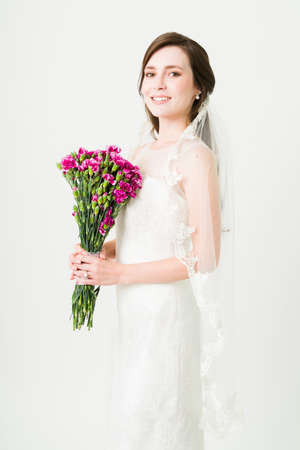 Gorgeous young bride posing in a beautiful wedding gown and a veil in front of a white studio backgroundの写真素材