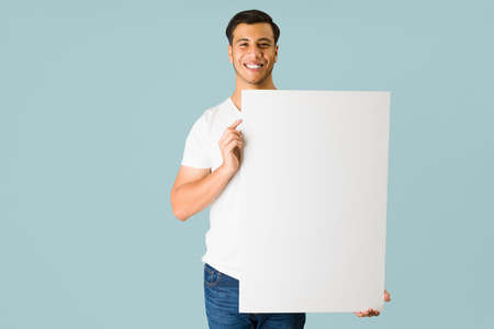 Handsome hispanic man looking at the camera and carrying a blank ad while promoting a great offer