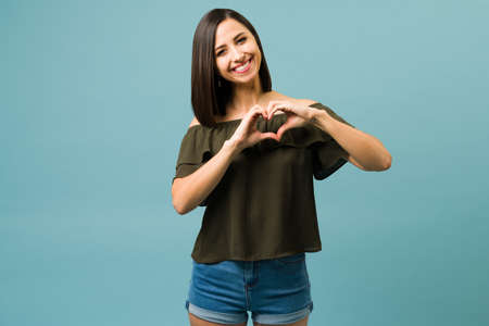 Adorable latin woman in love making a heart gesture with the hands in her heart