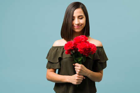Stop and smell the flowers. Relaxed beautiful woman carrying a bouquet of red flowersの写真素材