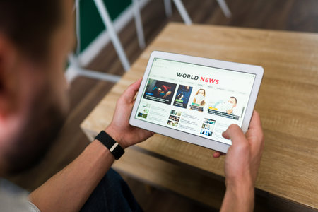 Smart man searching for a news article on his tablet. Adult man reading the news in an online...