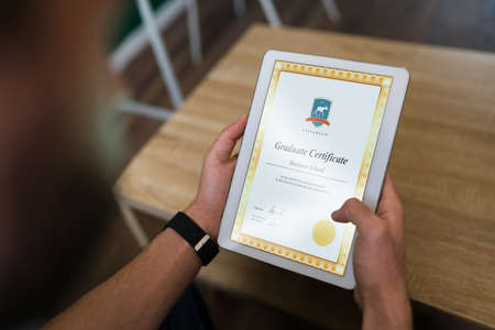 Online graduate certificate. Successful man receiving his college diploma in the tabletの写真素材