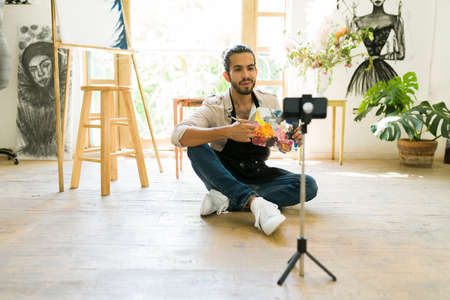 Young painter sharing tips online and recording a video tutorial with a smartphone to post on his social media channelの写真素材