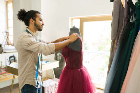 Talented young man putting a new finished gown in a manikin while enjoying her work as a fashion designerの写真素材