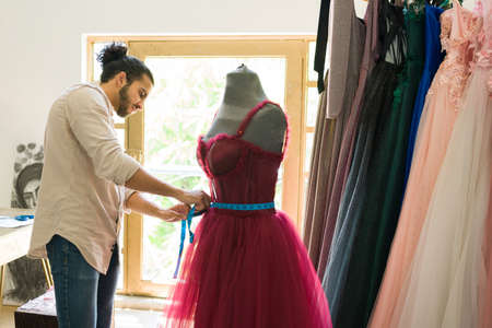 Hispanic fashion designer using a tape measure while making an elegant gown at the studioの写真素材
