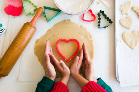 Close up of a mom and a little girl hands making a heart gesture while cutting and baking cookies