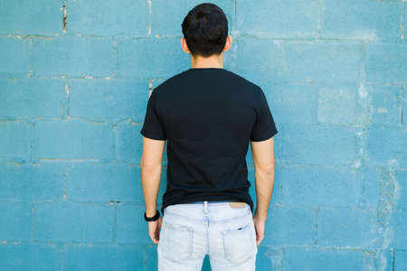 Hispanic man seen from behind showing the back of her black t-shirt with a design print