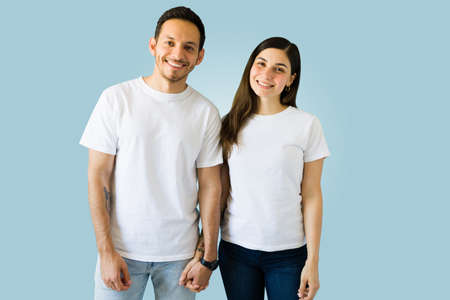 Happy boyfriend and girlfriend holding hands and looking at the camera while wearing matching print...