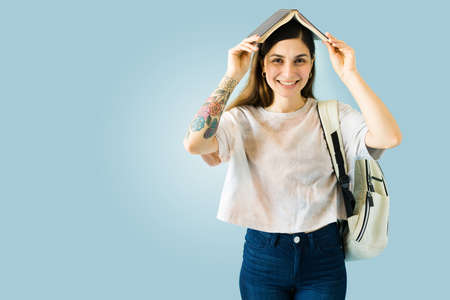 Playful young woman putting a book above her head and having fun while reading or studying for collegeの写真素材