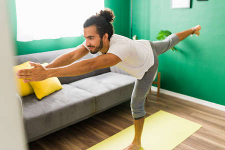 Feeling happy with yoga. Focused young man working on his balance while doing a warrior 3 pose at homeの写真素材