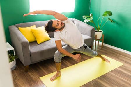 Sporty young man in a side angle yoga pose. Fit hispanic man exercising with yoga in the living roomの写真素材