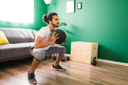 Strong handsome man with a healhty lifestyle doing squats exercises while holding a fitness ballの写真素材