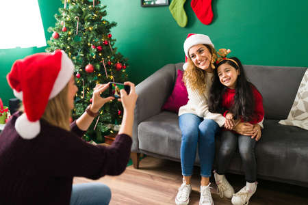 Happy woman taking a picture with a smartphone to her caucasian wife and daughter during Christmas eveの写真素材