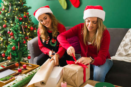 Attractive  couple smiling and using wrapping paper for their Christmas gifts next to their decorated treeの写真素材
