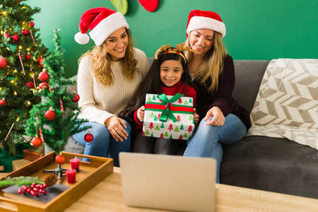 A gift from Santa. Excited little girl showing a beautiful present to family during a video call with her two mothersの写真素材