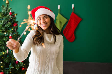 Having fun. Latin youn woman smiling and making eye contact while holding a lit sparkler during Christmasの写真素材