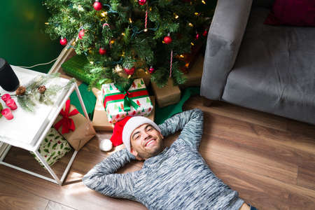 Top view of a cheerful young man smiling and relaxing next to the presents under the Christmas treeの写真素材