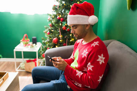 Texting my friends. Handsome young man preparing a Christmas party with family at homeの写真素材