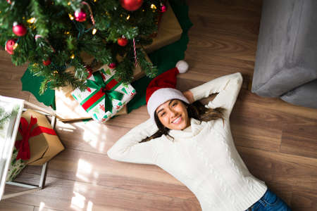 High angle of a happy young woman chilling and relaxing next to the presents under the Christmas treeの写真素材