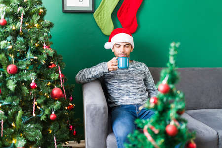 Cozy Christmas morning. Hispanic young man chilling at home and drinking hot chocolateの写真素材