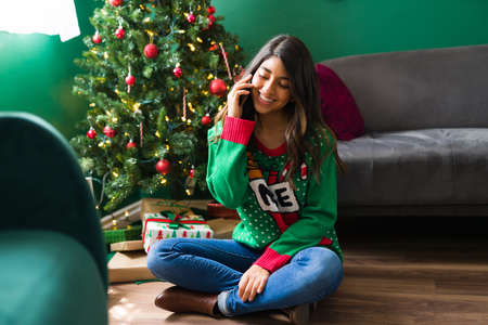 Latin woman talking on the phone with friends and waiting for family to start a Christmas partyの写真素材