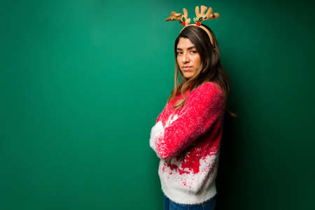 Feeling furious. Angry hispanic woman with crossed arms wearing a christmas hat against a studio backgroundの写真素材