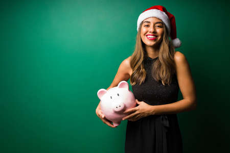 Beautiful young woman taking up the savings from a piggy bank to buy the christmas presentsの写真素材