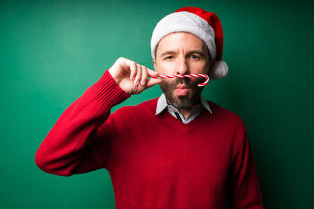 I love candy canes. Handsome hispanic man using a christmas candy cane as a mustacheの写真素材
