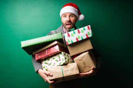 Worried and surprised hispanic man shopping for gifts and carrying a lot of christmas presentsの写真素材