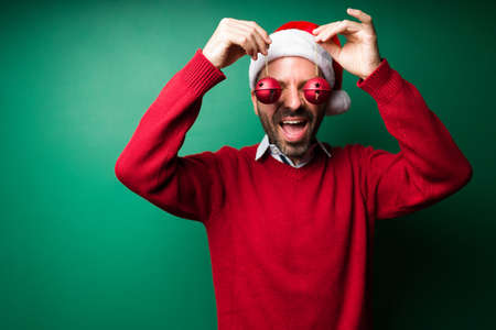 Fun young man playing with the christmas ornaments and laughing against a green backgroundの写真素材
