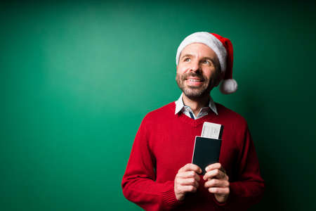 Dreaming of vacations. Smiling hispanic man holding his plane ticket and ready to travel during the Christmas holidaysの写真素材