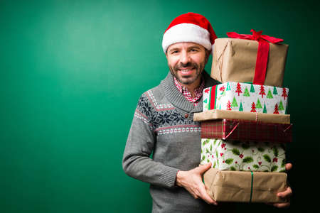 Ready to exchange gifts. Portrait of an attractive man holding a lot of christmas giftsの写真素材