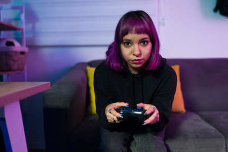 Portrait of an hispanic woman with purple hair holding a gamepad and focused on playing a video game matchの写真素材