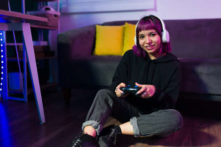 Relaxed beautiful gamer looking at the camera and smiling while playing video games at homeの写真素材