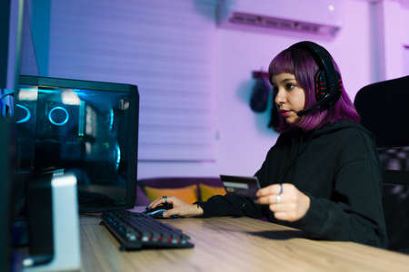 Attractive latin gamer paying for her online shopping with a credit card while sitting at the computerの写真素材