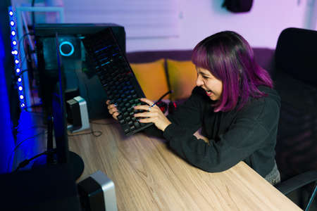 Latin female gamer feeling like a loser after playing an online video game and smacking the computer keyboardの写真素材