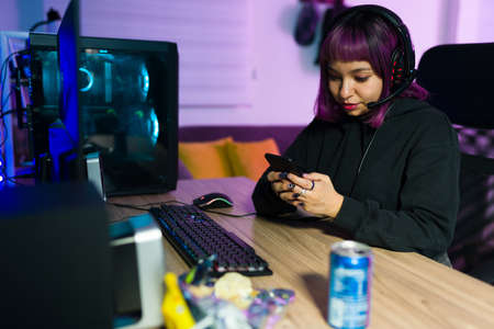 Happy young woman texting on her smartphone and smiling while taking a break from playing a video game onlineの写真素材