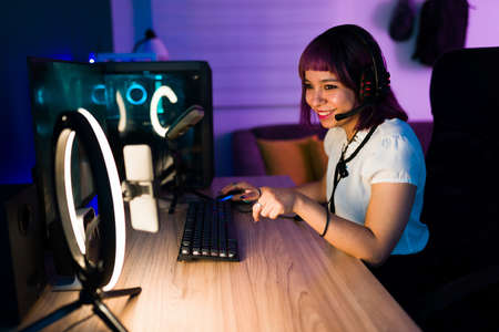 Excited attractive woman using a ring light and talking to her subscribers while live streaming playing video gamesの写真素材