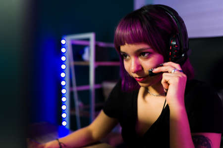 I am determined to win. Attractive young woman wearing a headset talking with her opponent while playing an online video gameの写真素材