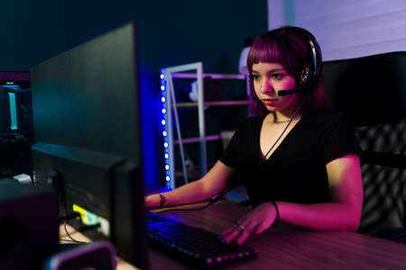 Attractive female gamer talking with her opponent on a headset while enjoying playing a video game on the computerの写真素材