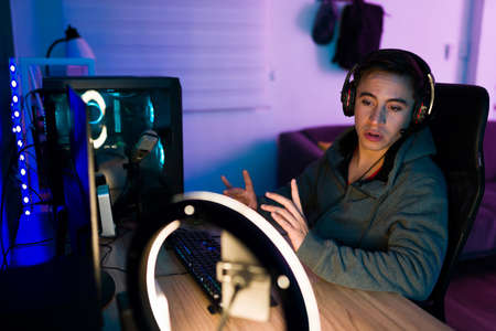 Handsome young man talking with his subscribers and followers during a live stream of his online video gameの写真素材