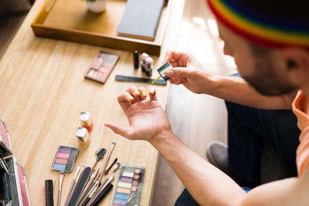 High angle of a gay man with a lot of beauty products painting his nails with a beautiful color and...