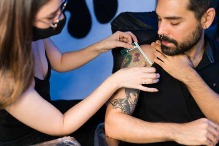 Young woman artist measuring a small tattoo on the arm of a male customer at her tattoo parlorの写真素材