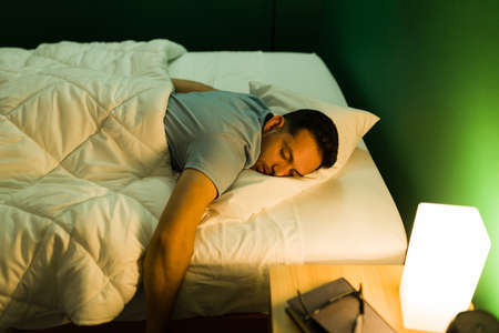 I'm so tired. Exhausted young man lying on his stomach and sleeping soundly in his bedroomの写真素材