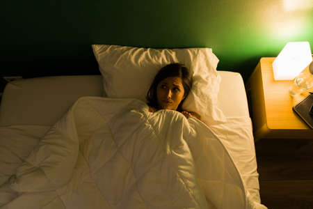 Scary sounds. Afraid young woman covering with the blanket and feeling scared after seeing horror moviesの写真素材