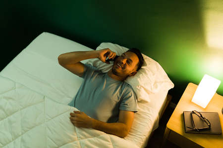 Top view of an attractive happy man speaking on the phone and enjoying a talk with his girlfriend before sleeping at nightの写真素材