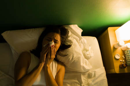 Feeling very sick. Ill woman with a cold and fever blowing her nose while lying in bed at night
