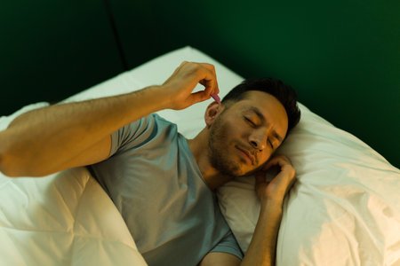 Attractive latin man with sleeping problems putting on ear plugs before sleeping at nightの写真素材