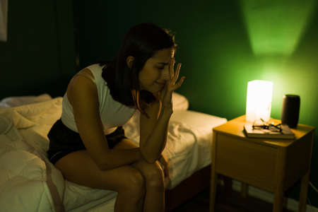 Depressed and heartbroken young woman in pajamas crying while feeling lonely in her bedroom