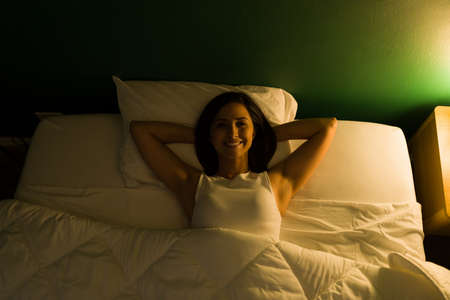 Cheerful young woman smiling and feeling relaxed while resting in her bedroom at night